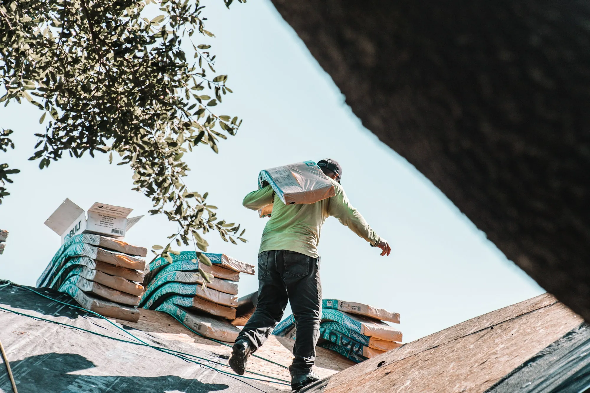 Roofer carrying a bundle of shingles across a roof with stacked shingle packs