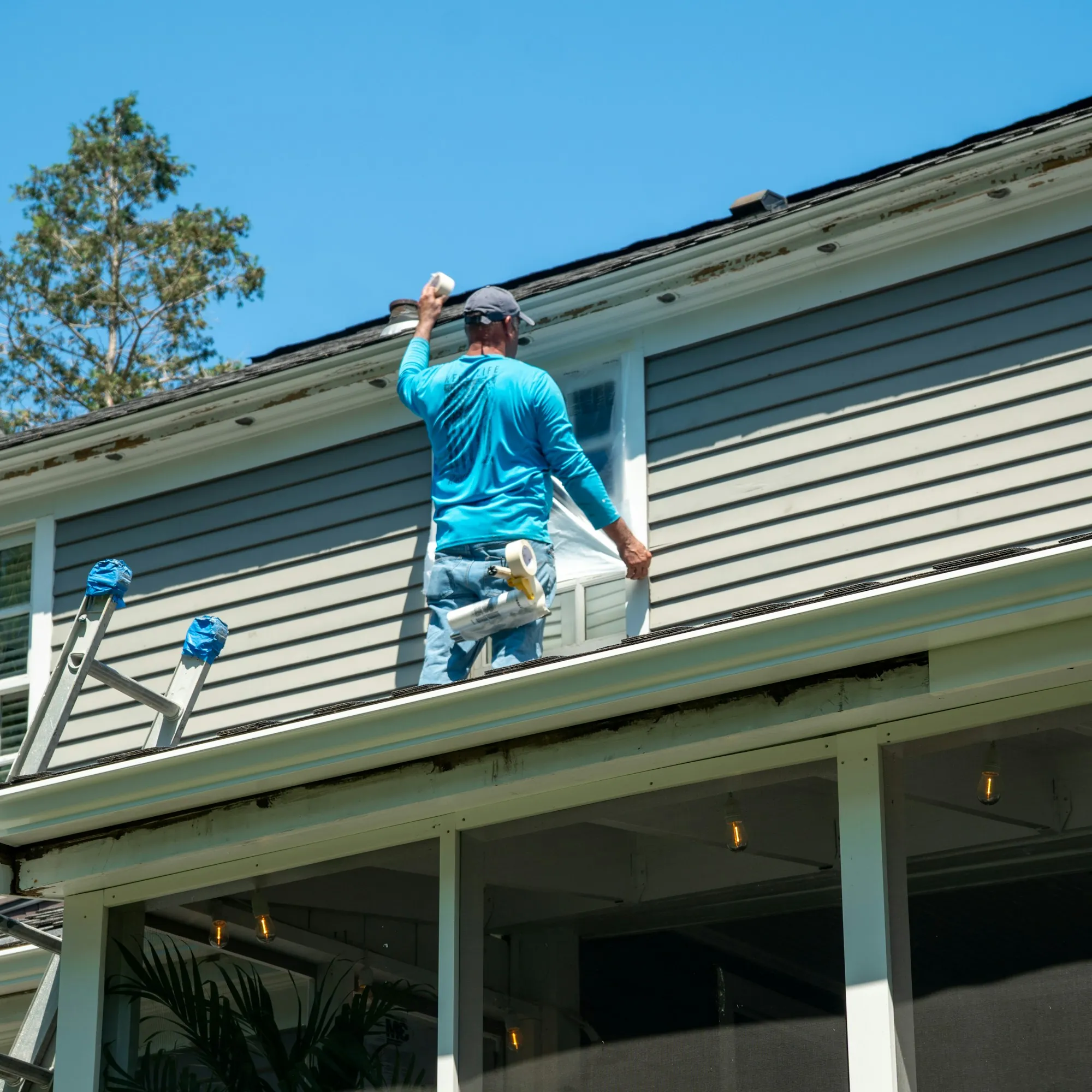 Worker on a porch roof covering a second-story window before roof work